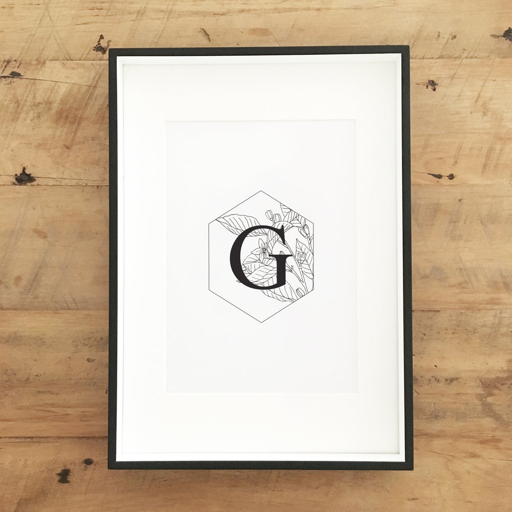 Black and white wall art in a frame with hexagon, floral outlines and the letter G.